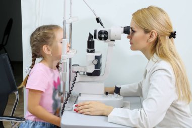Küçük kıza göz kliniği katında optometrist inceliyor.