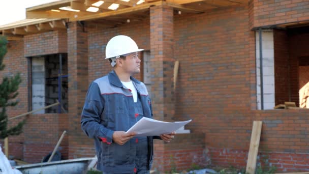 El hombre con el proyecto de pie en el sitio de la casa — Vídeos de Stock