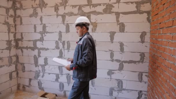Людина з паперами досліджує кімнату в будівлі, що будується — стокове відео