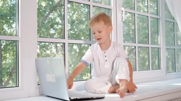 Маленький мальчик с ноутбуком на подоконнике — стоковое видео