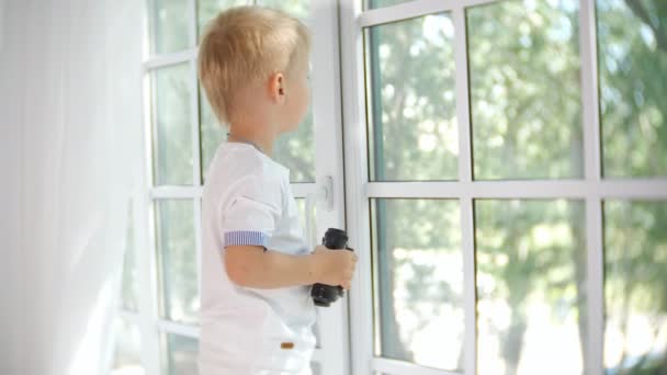 Little curious boy looking in window with binocular — Stock Video