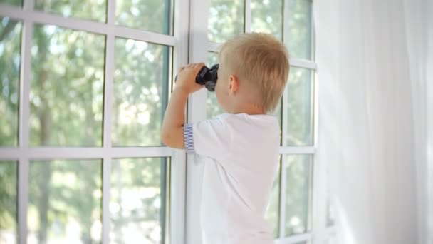 Nieuwsgierig jongetje op zoek in venster met verrekijker — Stockvideo