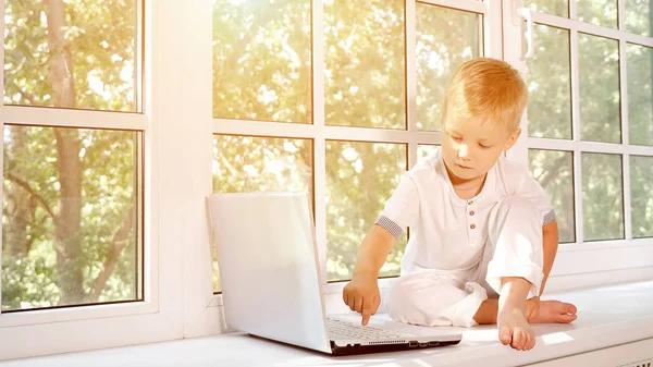 Liten pojke med laptop på fönsterbrädan — Stockfoto