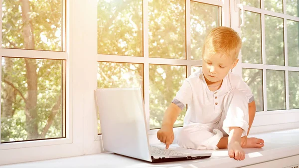 Menino com laptop na soleira da janela — Fotografia de Stock