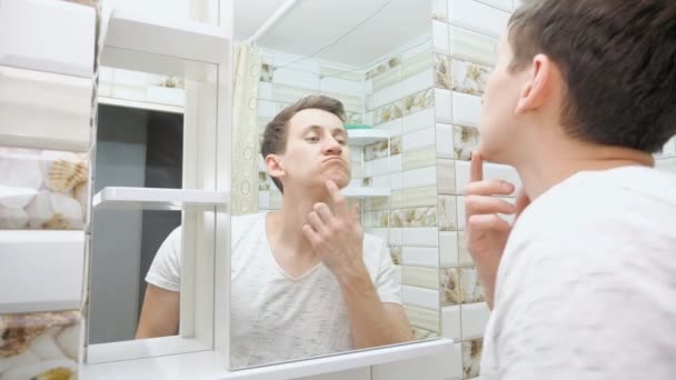 Молодой человек проверяет свою кожу в ванной комнате — стоковое видео