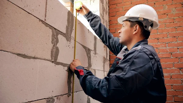 Man measuring length of window in building