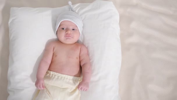 Dolce bambino in cappello e pantaloni sorridente mentre sdraiato su sfondo grigio — Video Stock