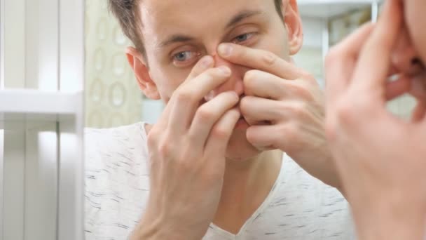 Close up van een jonge man permanent dicht bij een spiegel in de badkamer en een puistje knijpen op zijn gezicht — Stockvideo