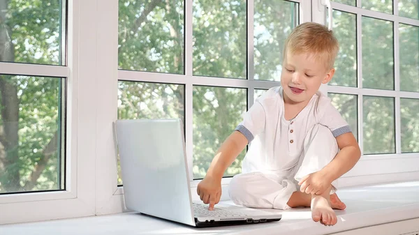 Liten pojke med laptop på fönsterbrädan — Stockfoto