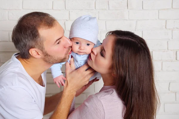 Beau homme et charmante femme embrassant bébé doux debout près du mur de briques blanches — Photo