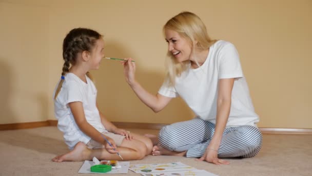 Γοητευτικά κορίτσια κάθονται στο πάτωμα με χαρτί και ακουαρέλα και μύτες ζωγραφικής μεταξύ τους έχοντας διασκέδαση — Αρχείο Βίντεο