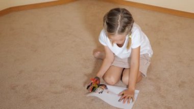 Kağıtları ile katta oturan ve evde suluboya ile çizim küçük kız