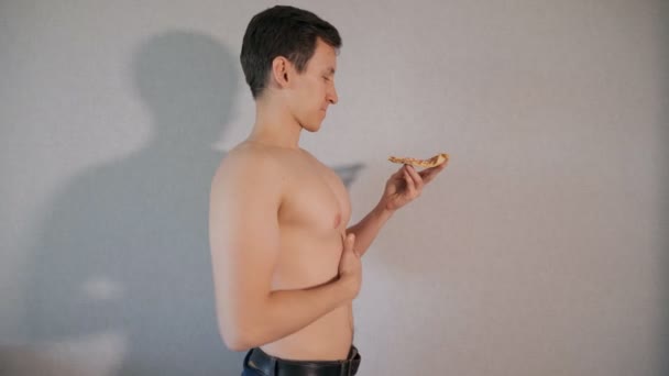 Νεαρός άνδρας με ένα κομμάτι πίτσα σε γκρίζο φόντο — Αρχείο Βίντεο