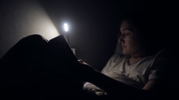 Ανάγνωση βιβλίων νεαρή γυναίκα στο κρεβάτι τη νύχτα σπίτι — Αρχείο Βίντεο