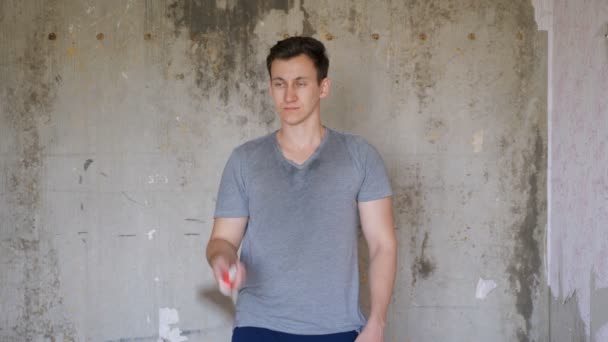 Мужчина, стоящий в комнате ремонта квартиры и жонглирующий лопаткой — стоковое видео