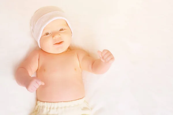 ยิ้มทารกหวานในหมวกและกางเกงขณะนอนบนพื้นหลังสีขาว . — ภาพถ่ายสต็อก