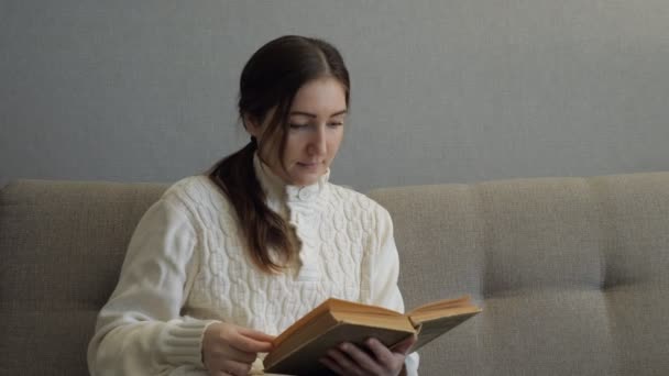 Menina bonita lendo um livro no sofá no interior acolhedor — Vídeo de Stock