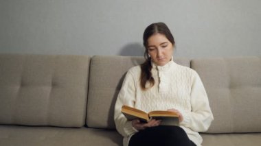 Güzel genç kadın kanepede oturan ve evde kitap okuma