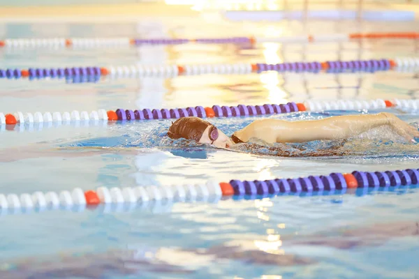 Jeune femme en lunettes et bonnet nage avant crawl course style dans la piscine intérieure de course d'eau bleue . — Photo