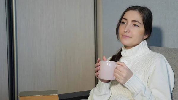 Młoda kobieta w ciepły sweter, siedząc na kanapie i i picie herbaty w domu — Zdjęcie stockowe
