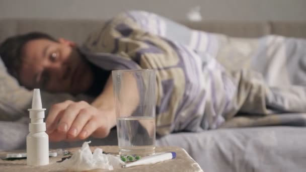 Молодой больной принимает упаковку таблеток, лежа дома на кровати — стоковое видео