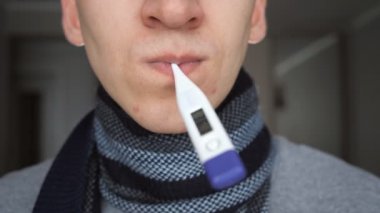 Dijital termometre ev, ağır çekim bulanık arka plan üzerinde dururken ağzına tutarak sıcak fularlı tanınmaz halde hasta adam