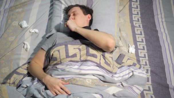 El hombre enfermo con gripe y secreción nasal se limpia la nariz con un pañuelo mientras está acostado en el sofá en casa. — Vídeo de stock