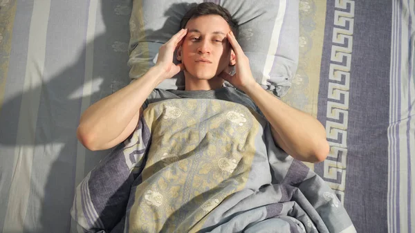 Больной человек трёт виски о кровать — стоковое фото