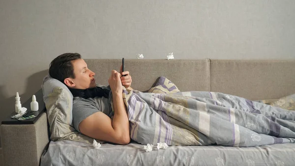 Hombre enfermo usando teléfono inteligente en el sofá — Foto de Stock