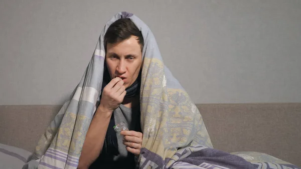 Hombre enfermo tomando pastillas bajo la manta — Foto de Stock