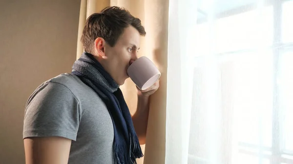 Больной человек с горячим напитком у окна — стоковое фото