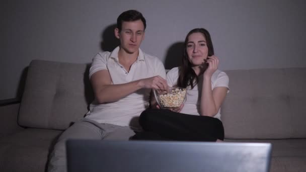 Щаслива пара дивиться фільм на телевізорі, сидячи на дивані вдома — стокове відео