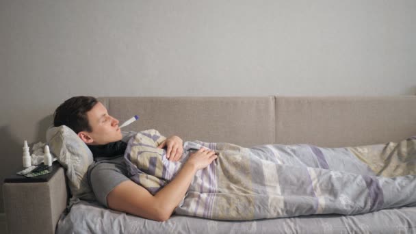Άρρωστος άνθρωπος με θερμόμετρο ξαπλωμένη στον καναπέ — Αρχείο Βίντεο