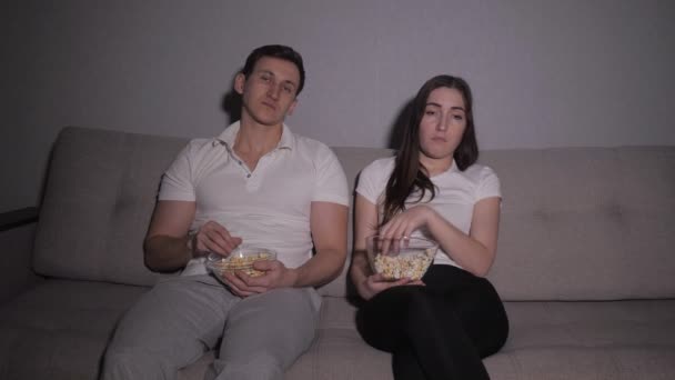 Tired and bored couple sitting lazily on a sofa at night watching tv — Stock Video