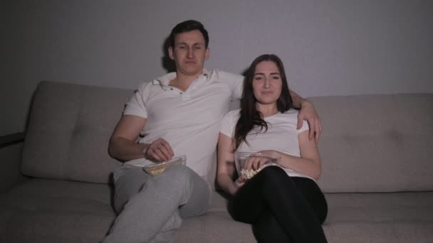 Ευτυχισμένο ζευγάρι βλέποντας μια ταινία στην τηλεόραση κάθεται σε έναν καναπέ στο σπίτι και τρώει ποπ κορν — Αρχείο Βίντεο