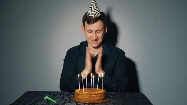 Веселый человек празднует праздник, сидит один за столом с тортом и свечами — стоковое видео