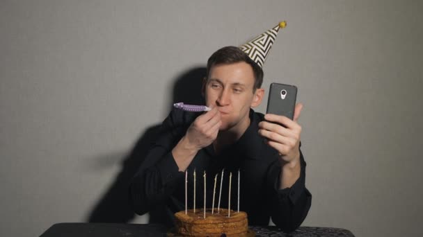 Jonge man met chocolade cake en een kaarsen met partij blowers en neemt selfie — Stockvideo