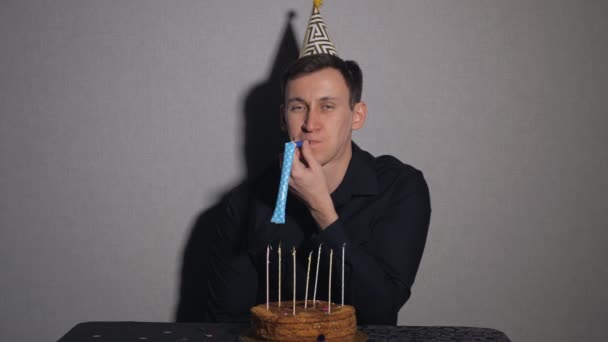 Junger Mann feiert einen Feiertag, er sitzt allein an einem Tisch mit Kuchen und Kerzen — Stockvideo