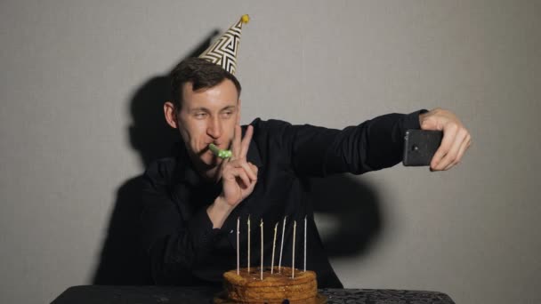 Junger Mann mit Schokoladenkuchen und Kerzen mit Partybläser und macht Selfie — Stockvideo