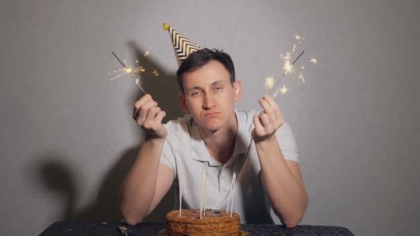 Sad lonely man in party hat celebrating birthday alone and holding the sparkler — Stock Video