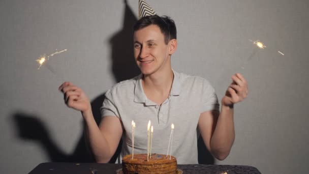 Nahaufnahme eines jungen Mannes mit Kuchen und einer Kerze, die die Wunderkerze hält. — Stockvideo