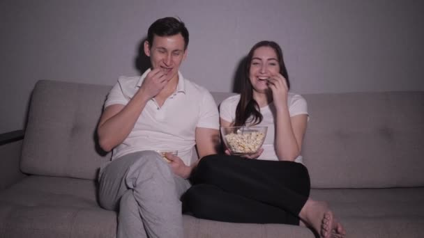 Casal feliz assistindo um filme na TV sentado em um sofá em casa — Vídeo de Stock