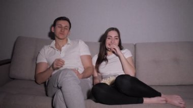 sıkılmış adam ve gülümseyen kadın kanepede oturup tv izlerken geceleri