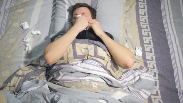 Ill uomo con influenza e naso che cola pulirsi il naso con un tessuto mentre sdraiato sul divano a casa — Video Stock