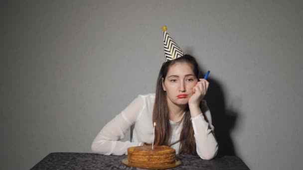 Одинокая грустная девушка празднует праздник, он сидит один за столом с тортом и свечами — стоковое видео
