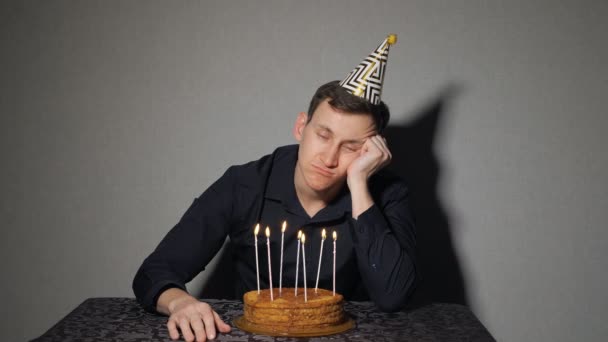 Hombre solo celebra una fiesta, se sienta solo en una mesa con un pastel y una vela — Vídeos de Stock