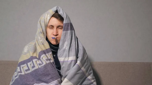 Больной человек в одеяле измеряет температуру — стоковое фото