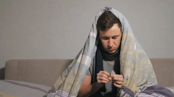 Hombre enfermo tomando pastillas bajo la manta — Foto de Stock