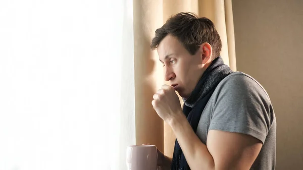 Больной мужчина с кружкой кашля возле окна — стоковое фото