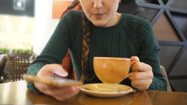 Chica sin rostro con un teléfono en la mano bebiendo café — Vídeos de Stock